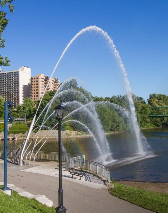 Water fountain over a river with city behind